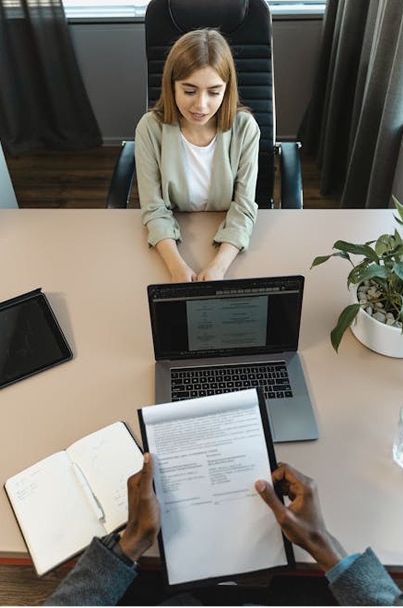 A woman sitting at a desk being interviewed by a man who is out of frame.